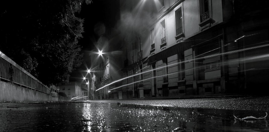 Schwarz-Weiß-Photo einer regennassen Straße bei Nacht.